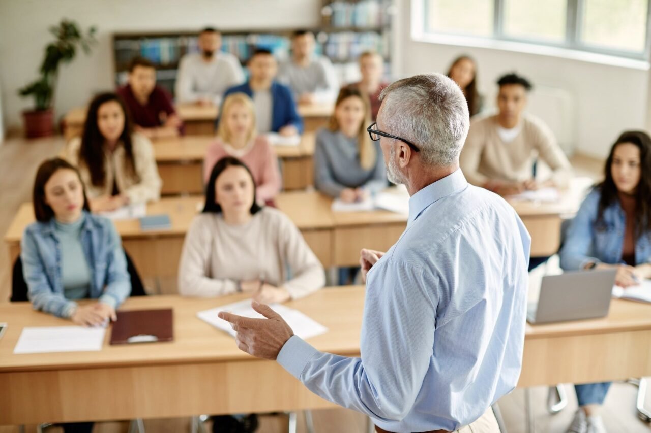 rear view of mature teacher talking to his student during lecture at university classroom .jpg